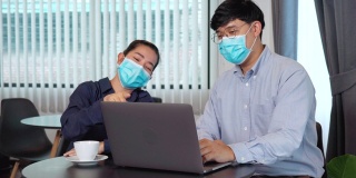 亚洲青年工商界人士戴着口罩在笔记本电脑上工作、讨论数据进行隔离防疫的4K视频