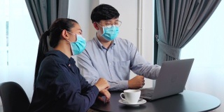 亚洲青年工商界人士戴着口罩在笔记本电脑上工作、讨论数据进行隔离防疫的4K视频
