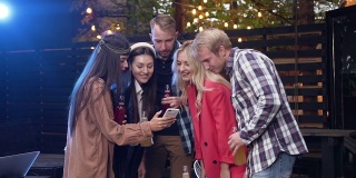 欢乐的男女朋友们在派对上用智能手机聊天，拿着酒瓶喝酒。在户外
