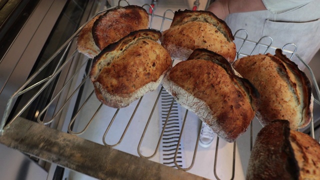 面包师把面包从烤箱中取出，放在架子上