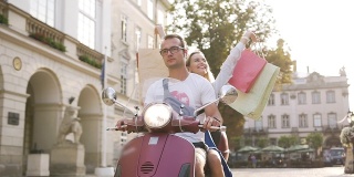 一对迷人的年轻夫妇骑着摩托车在城市街道上，快乐的女人举起手拿着买的东西