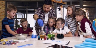亚洲科学老师与孩子们在实验课上进行实验，将干冰放入装有有色液体的烧瓶中，而两个烧瓶中的干冰会产生烟雾