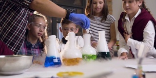 亚洲科学教师将干冰放入装有有色液体的烧瓶中，为六名学生做实验的正面图，在装有液体的烧瓶中有干冰产生的烟反应