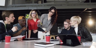 有创意的女性团队领导，站在桌边，在办公室开会时给年轻的创意团队指路。年轻商人的头脑风暴