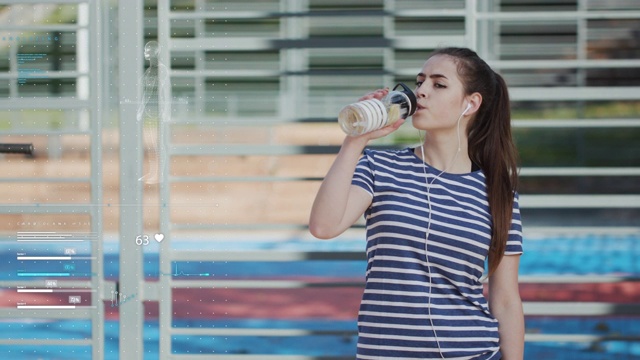 在运动设备的背景上，女运动员正在从一个搅拌器里喝水。智能技术移动应用健康运动跟踪虚拟图表屏幕显示DNA心脏健康信息