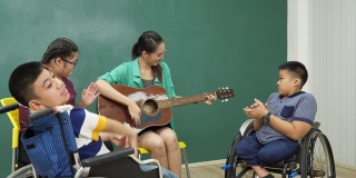 老师在教室里弹吉他陪着残疾儿童，非常开心