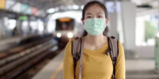 亚洲女性游客戴着口罩在站台上等候火车。