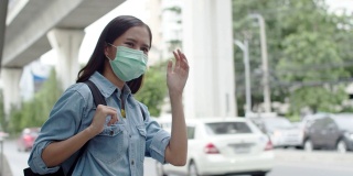 年轻的亚洲妇女戴着口罩站在公共汽车站白天。