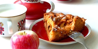 一块自制的苹果派放在盘子里，新鲜的苹果和一杯牛奶凑在一起