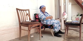 一位戴着头巾的亚洲老妇人坐在椅子上。
