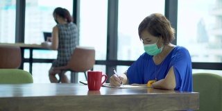 亚洲女员工戴口罩在商务办公室工作，与同事保持社交距离，以保护冠状病毒或covid-19疫情大流行。职场新常态政策