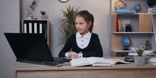 正面的笑容快乐的女学生制服坐在她的工作场所，用电脑做家庭作业