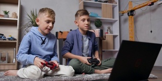 侧面的两个英俊的现代十几岁的男孩坐在地毯上，情绪上玩电脑上的视频游戏使用操纵杆