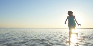 快乐的小女孩在日落的时候在大海里奔跑和享受