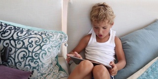 孩子们在平板电脑上玩游戏。坐在家里沙发上使用高科技平板电脑的孩子