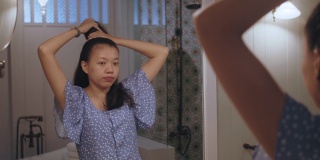 亚洲美丽的女人梳头和造型她的头发镜子在酒店室内背景浴室。4 k慢动作。