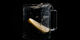 一片柠檬在慢镜头中落入一个装满清水的玻璃杯中。创造一种清爽的饮料。拍摄对象的概念。