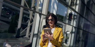 一个穿着西装的年轻女商人正在现代玻璃商务中心附近的平板电脑上工作。商业、技术和人的概念
