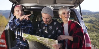 两名年轻女子和一名男子坐在汽车后备箱里用地图寻找正确的道路
