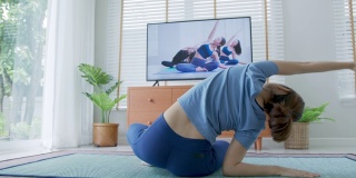 后视图:亚洲妇女伸展身体和瑜伽在客厅与宠物，看直播或视频电视在线教程。活动期间的隔离和社会距离的新常态概念。