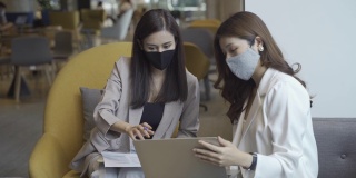 两位在办公室使用笔记本电脑开会的亚洲商务女性戴着医用口罩在办公室工作
