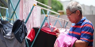 亚洲华人老人收集挂在前院清洗后的衣服