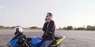 一个穿着皮夹克的年轻人坐在他的摩托车上，愉快地讲电话