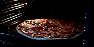 从烤箱内部看。用电热对流烤箱烹制意大利披萨。特写的披萨上面有西红柿，橄榄，马苏里拉火腿和奶酪。披萨奶酪融化冒泡。间隔拍摄。