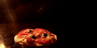 从烤箱内部看。用电热对流烤箱烹制意大利披萨。特写的披萨上面有西红柿，橄榄，马苏里拉火腿和奶酪。披萨奶酪融化冒泡。间隔拍摄。