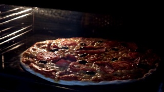 从烤箱内部看。用电热对流烤箱烹制意大利披萨。特写的披萨上面有西红柿，橄榄，马苏里拉火腿和奶酪。披萨奶酪融化冒泡。间隔拍摄。视频素材模板下载