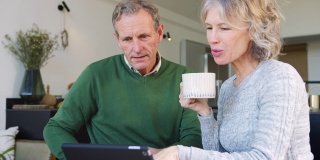 退休老年夫妇在家使用数字平板电脑在线购买产品或服务