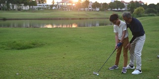 日落时分，一位亚洲华人老人在高尔夫球场上教孙子如何打高尔夫