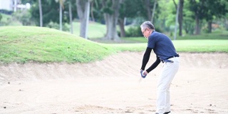 一位亚洲的中国资深高尔夫球手用他的铁棒在沙坑里打他的高尔夫球
