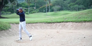 一位亚洲的中国资深高尔夫球手用他的铁棒在沙坑里打他的高尔夫球