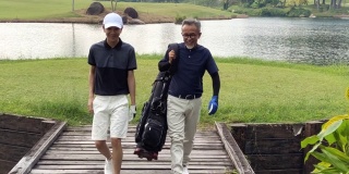 一名亚洲华人男子带着十几岁的儿子往高尔夫球场走去，手里拿着高尔夫球袋看风景