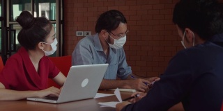 新概念的正常办公商务人士企业员工戴着防护口罩坐在办公室开会工作