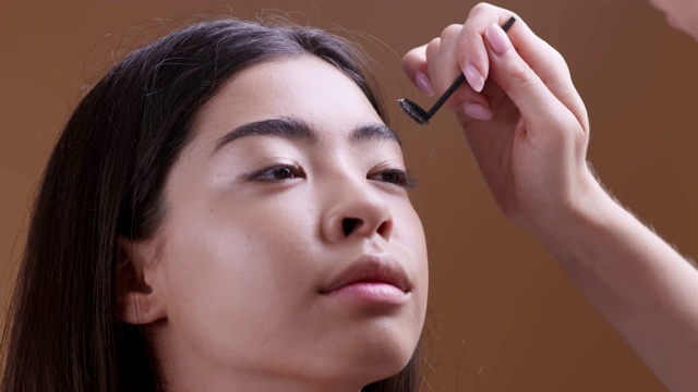 化妆师为年轻的亚洲女孩做美丽的眉毛，近距离