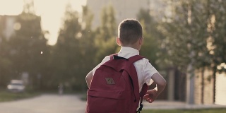 跟踪，慢动作:一个男生放学后跑回家。他身后是一个书包。