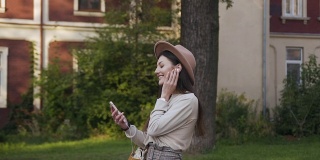 30岁的女孩戴着时髦的帽子，戴着耳机，站在房子的院子里欣赏音乐