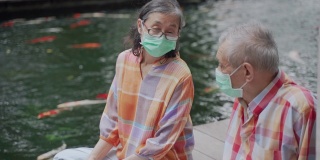 一对亚裔华人老年夫妇戴着外科口罩坐在地板上聊天