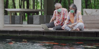 一对亚洲老年夫妇戴着外科口罩坐在地板上聊天