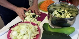 一个男人在磨蔬菜骨髓。附近的蔬菜，烹饪南瓜鱼子酱。桌上放着西葫芦、胡萝卜、洋葱和西红柿。