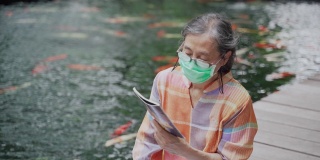 一名亚裔华裔老年妇女戴着医用口罩坐在地板上看书