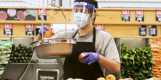 蔬菜水果店的员工戴着防护面罩、面罩和防护手套把苹果放在磅秤上