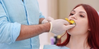 正牙医生将一个装有硅胶材料的勺子放入病人的嘴里，以给她的牙齿做一个印模
