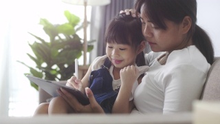 孩子在线学习的数字平板电脑与她的母亲在家里视频素材模板下载