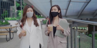 两个亚洲女商人拿着咖啡杯边走边谈生意
