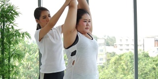 超重肥胖的亚洲妇女在垫子上与女教练练习瑜伽来减肥