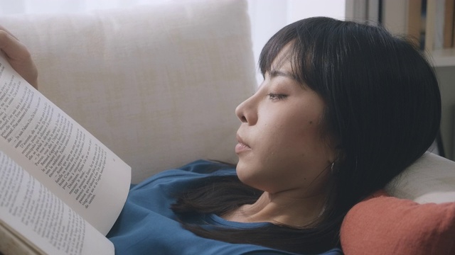 一个女人躺在沙发上看书。缓慢的运动。