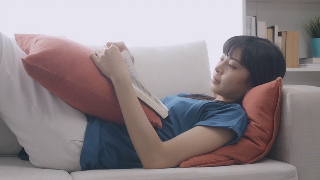 一个女人躺在沙发上看书。慢镜头，中速镜头。